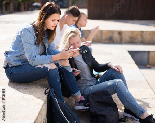Photography teenagers play in smartphones in schoolyard