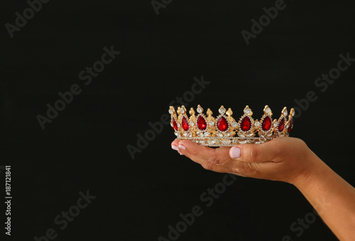 Woman's hand holding a crown for show victory or winning first place over black background.