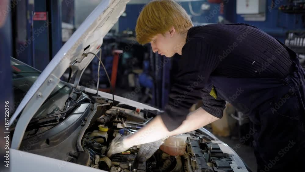 auto mechanic is disassembling an energy unit from inner structure of car in an dark workshop of auto-service auto mechanic is disassembling an energy unit from inner structure of car in an dark workshop of auto-service