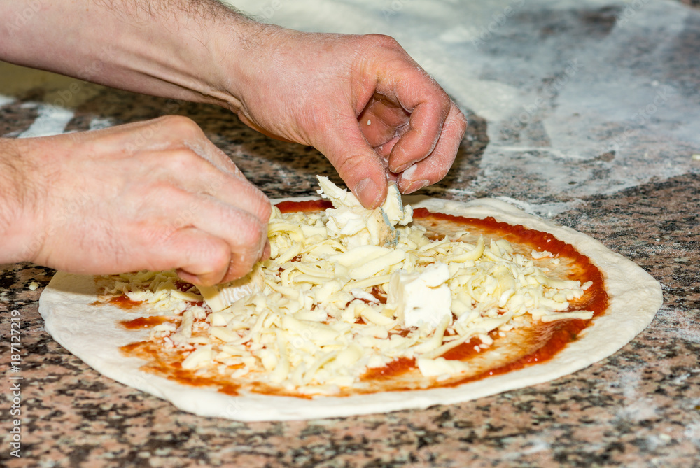 Fresh original Italian raw pizza, dough preparation in traditional style: the chef distributes the cheese. Food, italian cuisine and cooking concept.