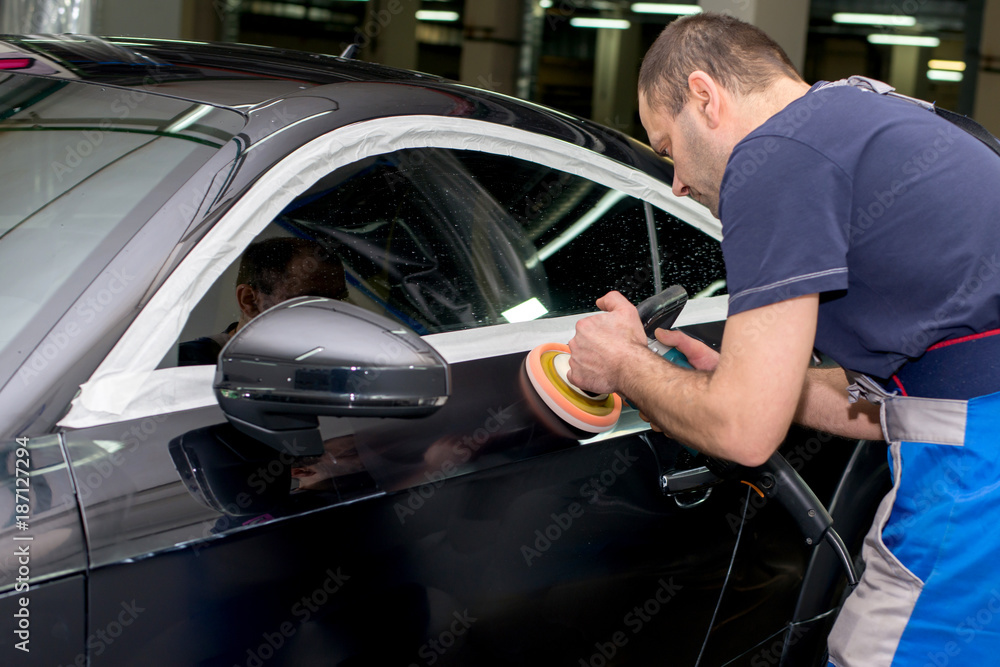 A man polishes a black car with a polisher A man polishes a black car with a polisher