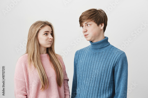 Фотография Waist up portrait of young female and male wearing knitted colourful sweaters having discontent looks pouting cheeks