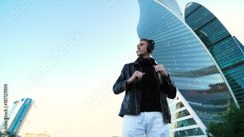 Young handsome man listening to music with pro headphones and dance in the city strreet 4K photo
