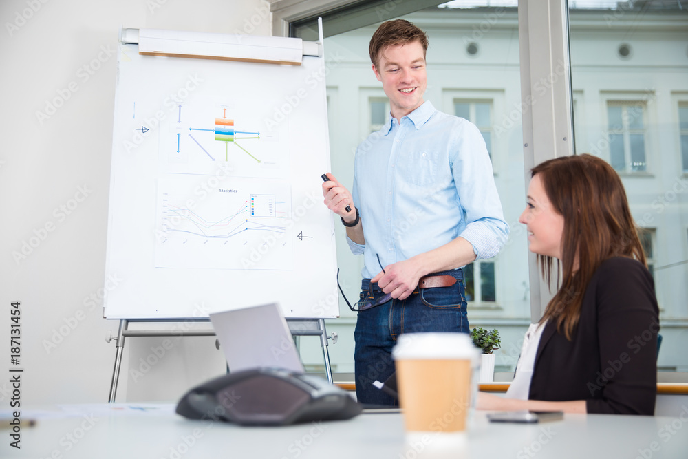 Smiling Businessman Giving Presentation To Colleague In Office Smiling Businessman Giving Presentation To Colleague In Office