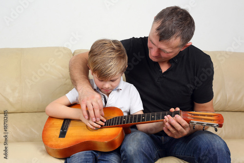 father teaches his son to play the guitar