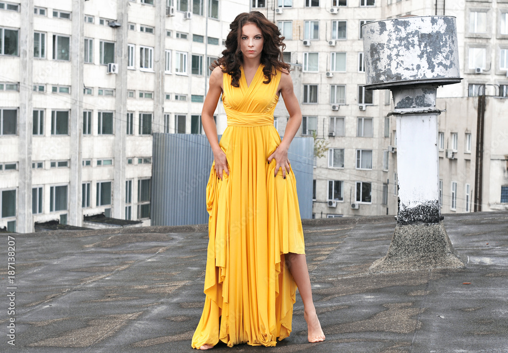 Young girl in a long yellow dress on the roof of a building in the city.
Fashionable model on the roof of the house