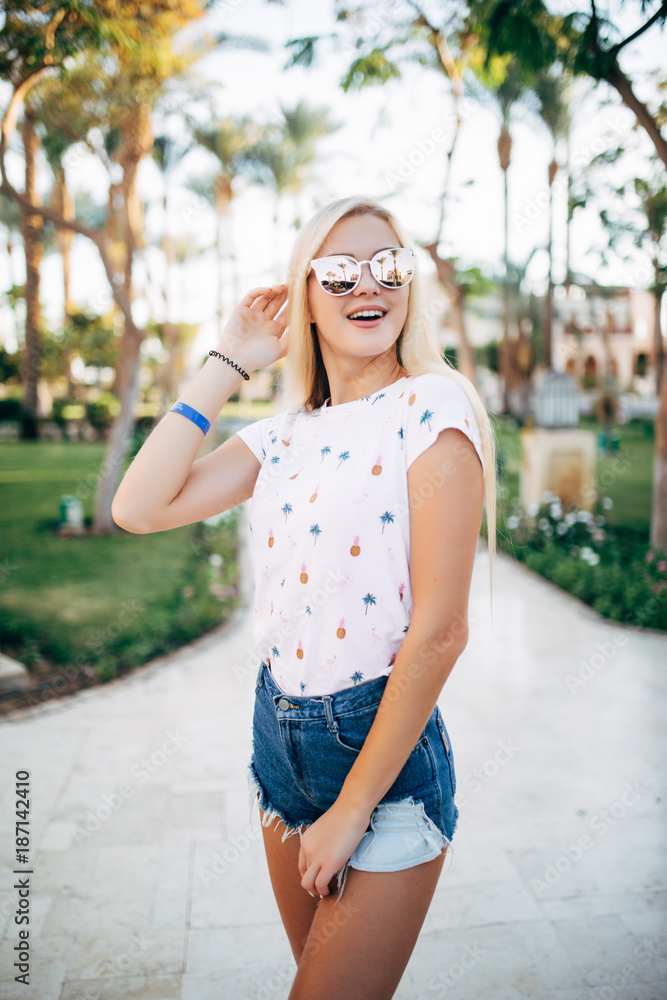 Naklejka premium Relaxed happy smile young woman in sunglasses on terrace of hotel on palms background. Summer vocation
