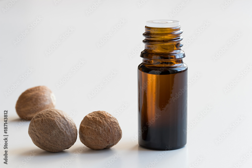 A bottle of nutmeg essential oil with nutmeg seeds on white background A bottle of nutmeg essential oil with nutmeg seeds on white background