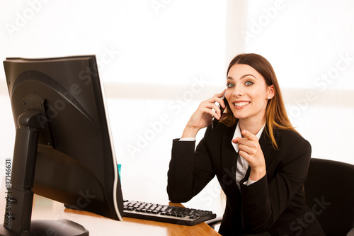 Beautiful business woman talks on smert phone in office at her desk photo