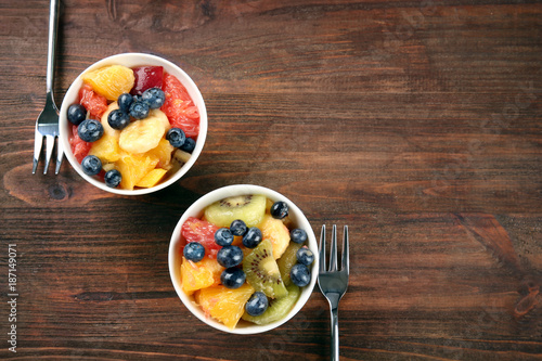 Bowls with delicious fruit salad on wooden table