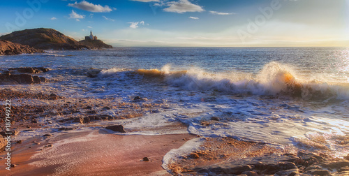 Back lit waves at Bracelet Bay, featuring the Mumbles Lighthouse on the Gower peninsula in Swansea, South Wales, UK
