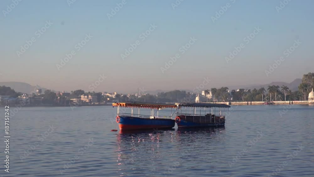Boats tied in the middle of a lake with mountains in the distance. Shot at the Fateh Sagar or Pichola lake in Udaipur the beautiful blue water, mountains in the distance and colorful boats showcase