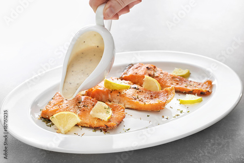 Pouring sauce onto tasty rainbow trout fillets on plate photo