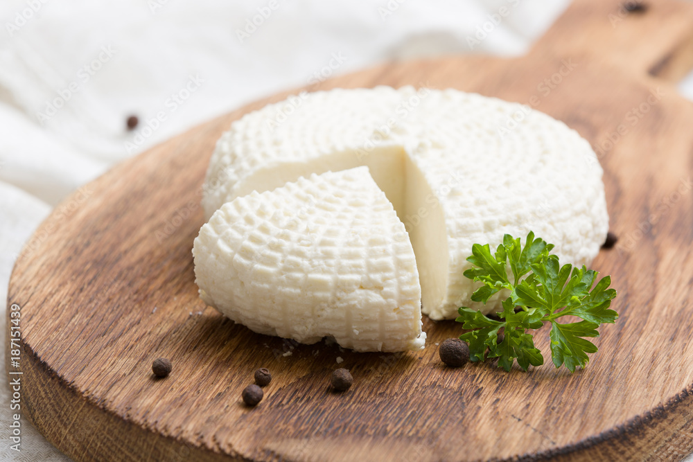 Sliced round white homemade cheese - traditional milk creamy dairy product on vintage wooden board. Rustic style. Sliced round white homemade cheese - traditional milk creamy dairy product on vintage wooden board. Rustic style.