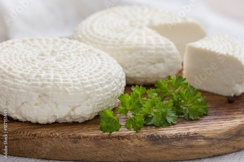 Sliced round white homemade cheese - traditional milk creamy dairy product on vintage wooden board. Rustic style.
