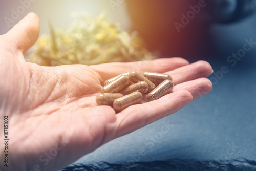 Herbal capsules in woman hand black stone background