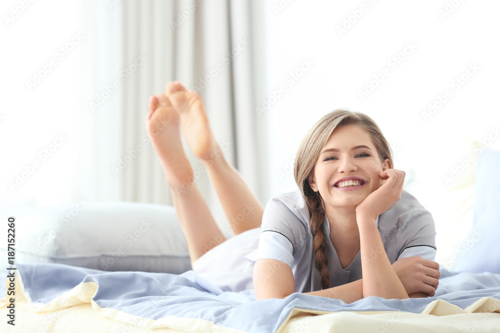 Young chambermaid in uniform resting on bed indoors Young chambermaid in uniform resting on bed indoors