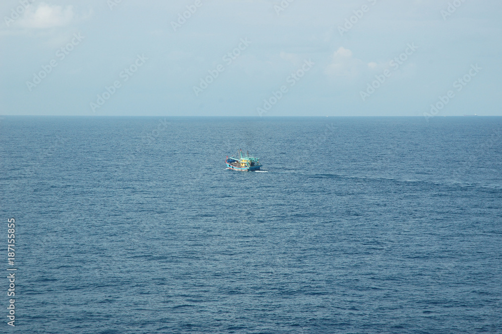 A fishing boat heading out to sea. The sea is calm and the sky pale blue with faint clouds.