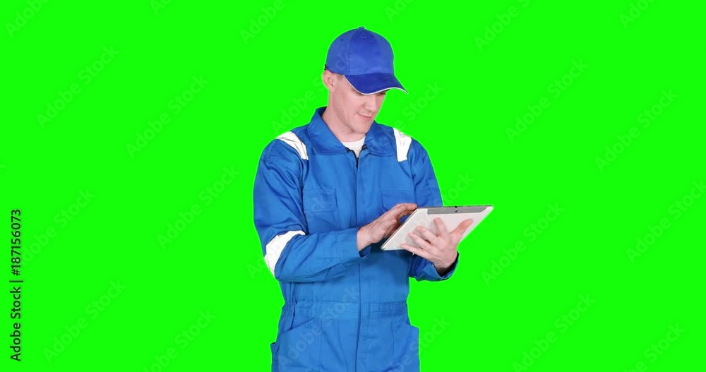 Caucasian car mechanic working with a digital tablet and wearing blue uniform, shot in 4k resolution with green screen background Caucasian car mechanic working with a digital tablet and wearing blue uniform, shot in 4k resolution with green screen background