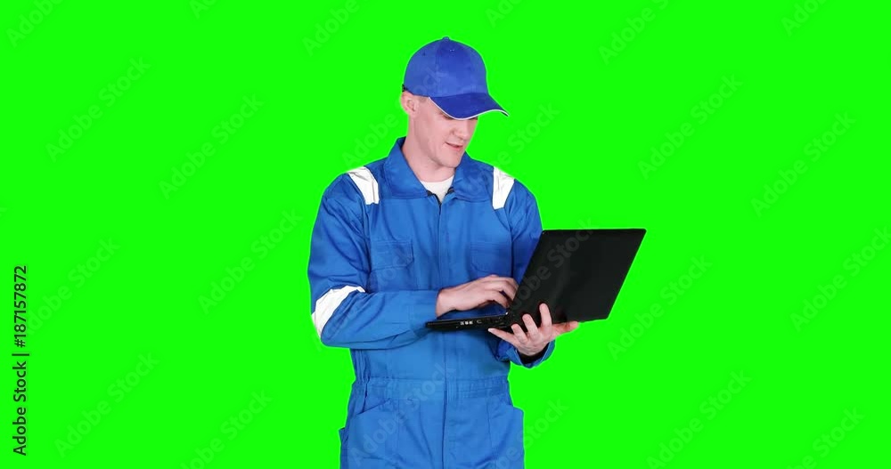 Male Caucasian auto mechanic working with a laptop computer while wearing blue uniform and standing in studio, shot in 4k resolution with green screen background Male Caucasian auto mechanic working with a laptop computer while wearing blue uniform and standing in studio, shot in 4k resolution with green screen background