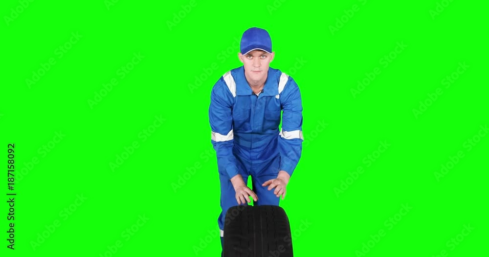 Caucasian auto mechanic pushing a tire in the studio while wearing blue uniform, shot in 4k resolution with green screen background Caucasian auto mechanic pushing a tire in the studio while wearing blue uniform, shot in 4k resolution with green screen background