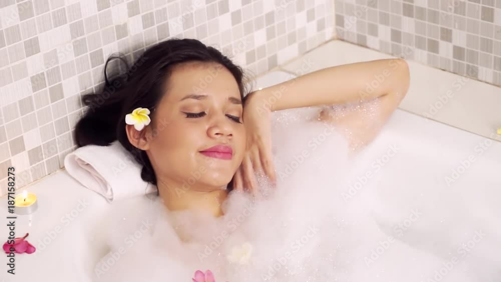 Spa treatment concept. Attractive woman relaxing in bathtub with foam and frangipani flowers Spa treatment concept. Attractive woman relaxing in bathtub with foam and frangipani flowers