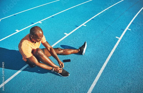 Obraz Młody zawodnik wiążący wcześniej swoje buty na bieżnię