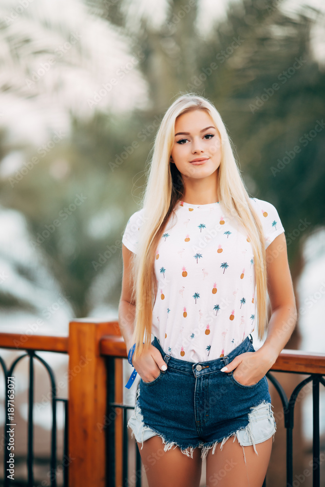Cute happy girl enjoys summer vacation on resort. Portrait of cheerful young woman in white shirt standing on terrace on amazing ocean background Cute happy girl enjoys summer vacation on resort. Portrait of cheerful young woman in white shirt standing on terrace on amazing ocean background