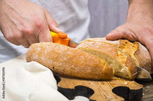 Man's hands cutting bread on the wooden plank.