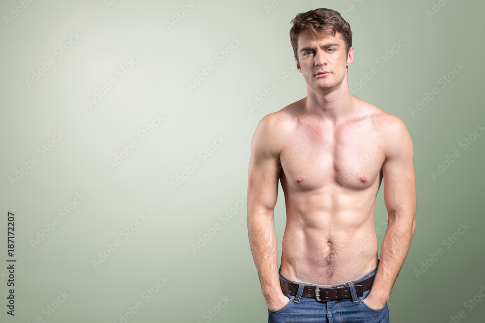 Young fit man topless in blue jeans posing