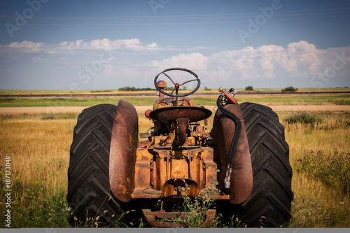 The back end of a rusted vintage tractor facing out toward fields under cloudy sky in a rural black and white summer countryside landscape
