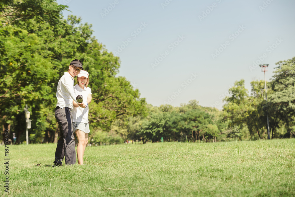 Asian couple playing golf. man teaching woman to play golf while standing on field Asian couple playing golf. man teaching woman to play golf while standing on field
