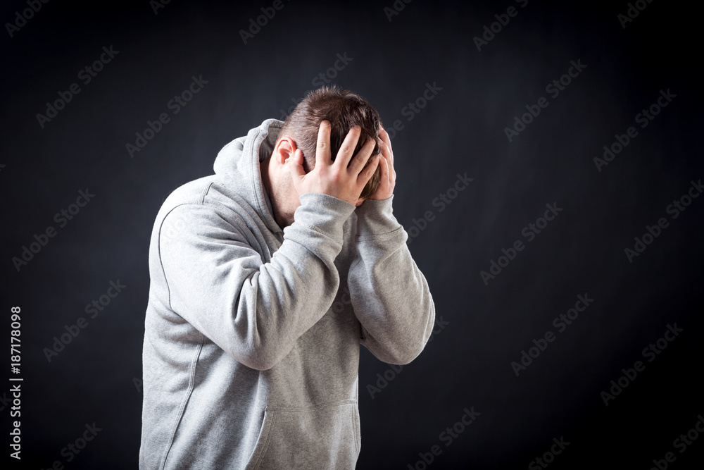 A young dark-haired man in a sporting gray sweatshirt is upset, upset and keeps his hands on his head on a black isolated background, the torturer suffers a headache A young dark-haired man in a sporting gray sweatshirt is upset, upset and keeps his hands on his head on a black isolated background, the torturer suffers a headache