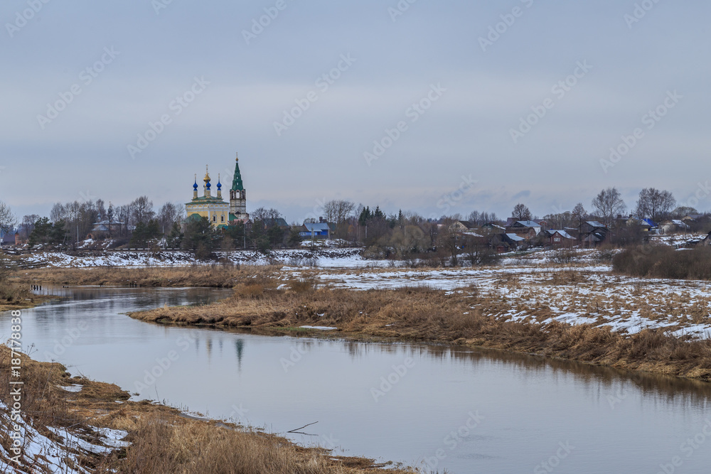 The village on the bank of the river in late autumn, on the banks of snow and dry grass
