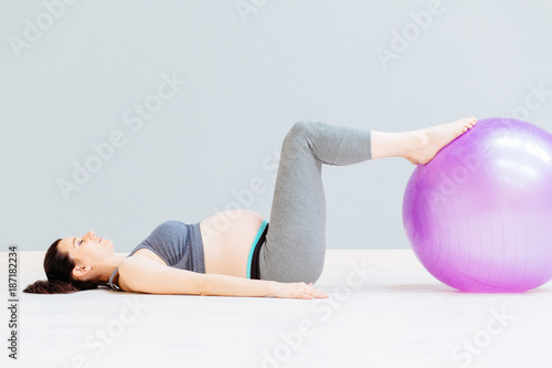 Seria photo of a pregnant fitness woman doing relaxing exercises with fitball while lying on the floor indoor. Working out and fitness, pregnancy concept.