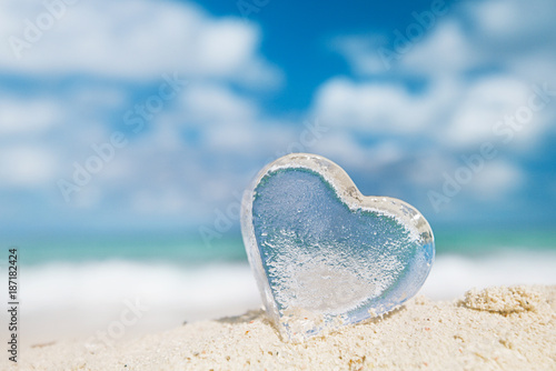 clear glass heart on white sand beach,