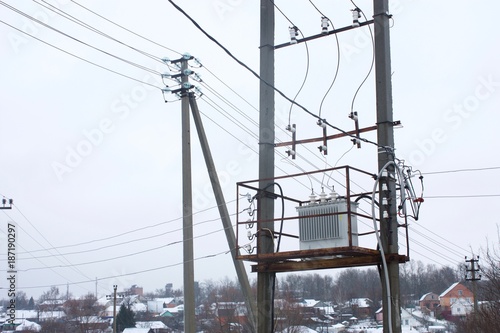 electrical distribution transformer on concrete pillars in the background of the rural settlement in winter