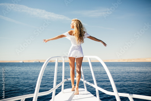 Woman standing on the nose of the yacht at a sunny summer day, breeze developing hair with open arms beautiful sea on background © F8  \ Suport Ukraine