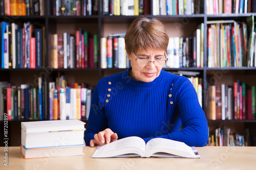 Happy senior woman  with books in library.