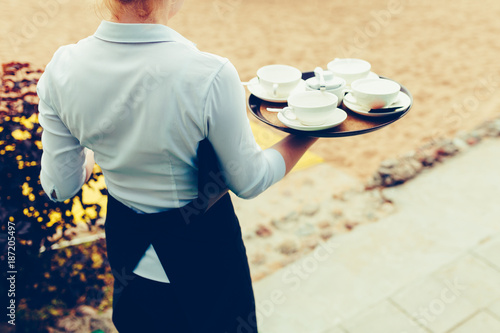 A waiter carries on a brown tray of food on the beach background Hot snacks on the tray. The wait staff serving the tables at the event or holiday. Vintage tonted photo. photo