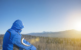 a tourist man standing with his back looking at the mountains at dawn. winter. warm blue jacket with a hood