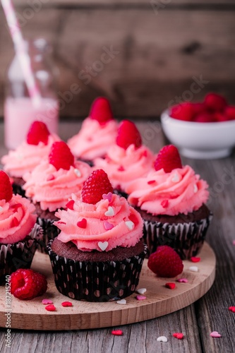 Chocolate cupcakes with pink cream, sugar hearts and fresh raspberries for Valentine Day
