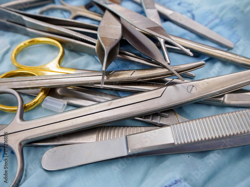 Close-up detail of a pile of surgical instruments, including metzenbaum and mayo scissors, adson forceps, and scalpel handles on a sterile drape. Healthcare and surgery concept. photo