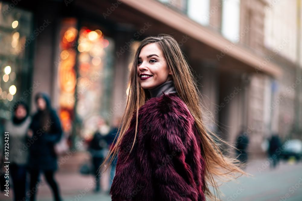 Young beautiful model girl smiles and looks back in the city. Dynamically young girl walks down the street.Hair fluttering in the wind.