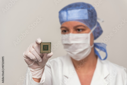 Female laboratory coworker holds in hand a digital CPU processor microchip in a lab. Electronic engineer is wearing protective clothing. Concept: computer and technology or computer security