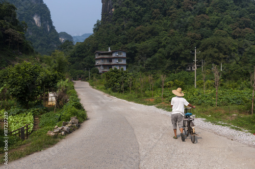 Yangshuo, China - August 2, 2012: Man with a bicycle in a contry road near the town of Yangshuo in China, Asia, with the tall limestone peaks on the background