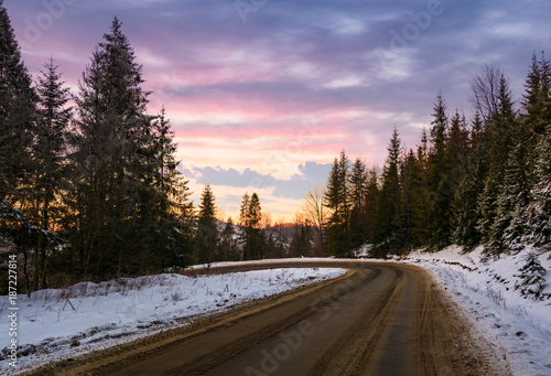 road through winter forest at dusk. lovely transportation scenery in mountains with snowy hills © Pellinni