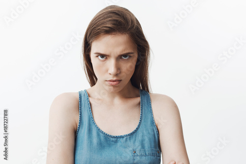 Close up of agressive attractive young caucasian woman with dark long hair in blue shirt looking in camera with angry face expression, being mad after husbend come home drunk with lipstick on his neck