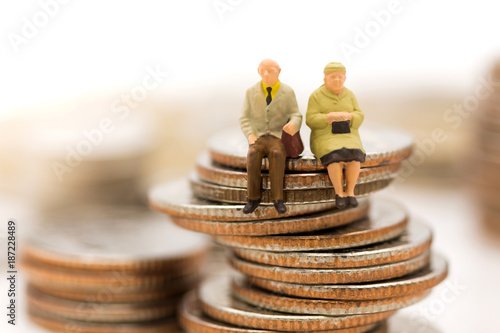 Miniature people, Old couple figure sitting on top of stack coins using as background retirement planning, Life insurance concept.