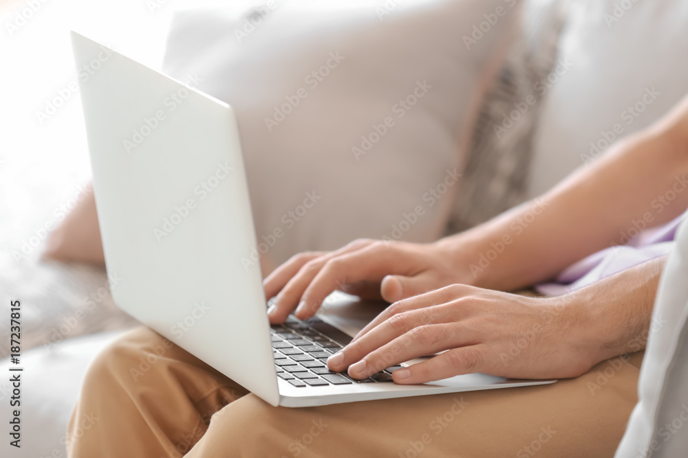 Young man using his laptop while sitting on sofa indoors Young man using his laptop while sitting on sofa indoors